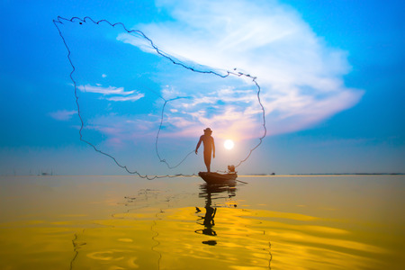 Silhouettes fisherman throwing fishing nets during sunset, Thailand.の写真素材