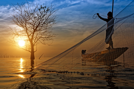 Silhouettes fisherman throwing fishing nets during sunset, Thailand.の写真素材