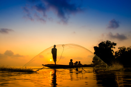 Silhouettes fisherman throwing fishing nets during sunset, Thailand.の写真素材