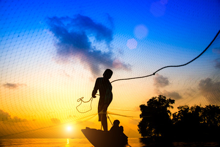 Silhouettes fisherman throwing fishing nets during sunset, Thailand.の写真素材