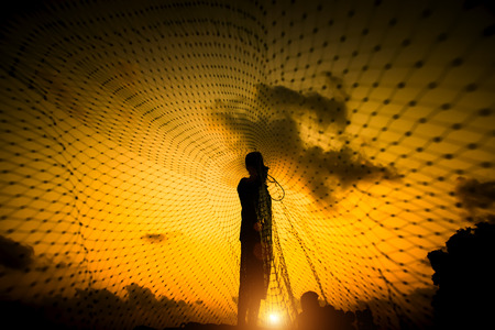 Silhouettes fisherman throwing fishing nets during sunset, Thailand.の写真素材