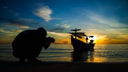 Silhouette of un-focus photographer shooting fishing boat on the beach.