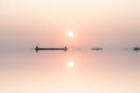 Mirror image of silhouette fisherman with sunset sky on the lake.の写真素材