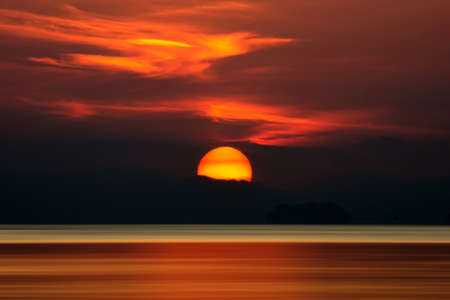 Big sun and orange cloud in sunset sky on the lake.の写真素材