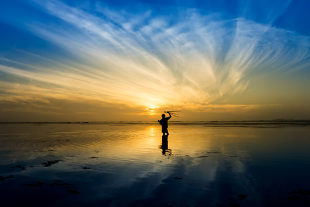 Minimal Silhouette of happy tourist with poles in hand above head on the beach with sunrise sky.の写真素材