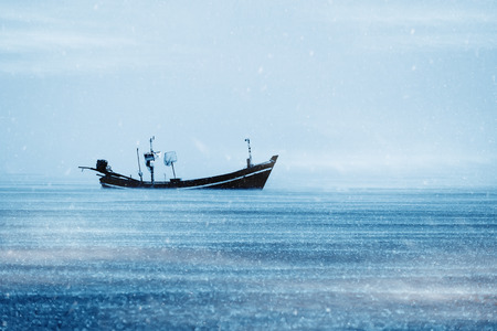 Fishing boat on the sea with snowfall with mist in winter color tone.の写真素材