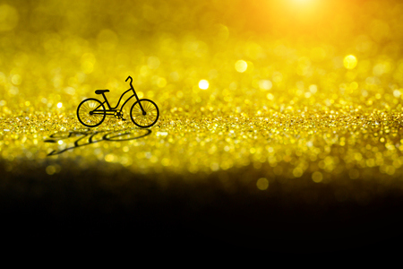 Silhouette of a bicycle on gold sparkling Glitter bokeh Background.の写真素材
