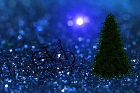 Silhouette of a bicycle in christmas night with blue sparkling glitter bokeh background and pine tree.の写真素材