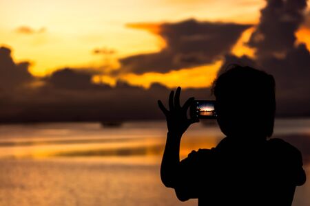 Silhouettes a women are use phone shooting the sunset at the lake.の写真素材