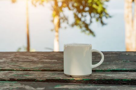 White coffee mug on the wooden in the morning time with sunlight.の写真素材