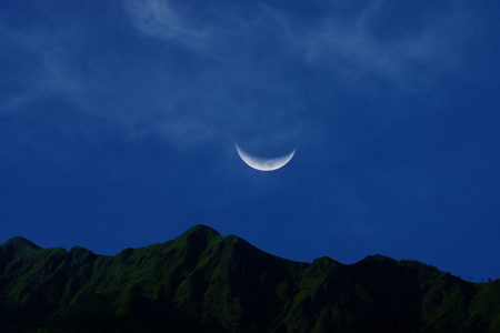The crescent moon rising in the blue sky with soft cloud over the mountain.の写真素材