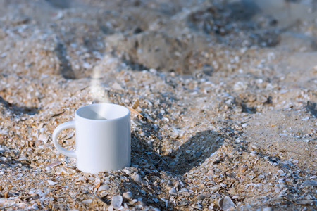 White mug coffee on the sand.