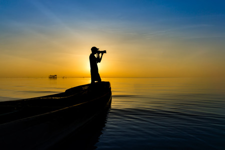 Black shadow of photographer and fishing boat on the lake with sunrise sky.の写真素材