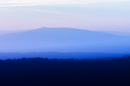 Soft silhouette of blue mountain with empty sky and soft mist in blue color tone.の写真素材