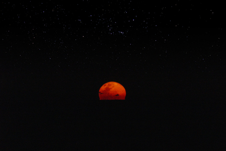 Red moonrise in the dark night above the black sea with star on top.
