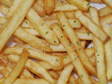 Close up of French Fries Potato Cooking Deep Fried in Hot Oil with salt and dry parsley leaf.