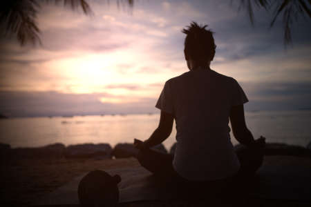 The silhouette of a beautiful woman practicing yoga on the beach during the red and orange summer sunset.の写真素材