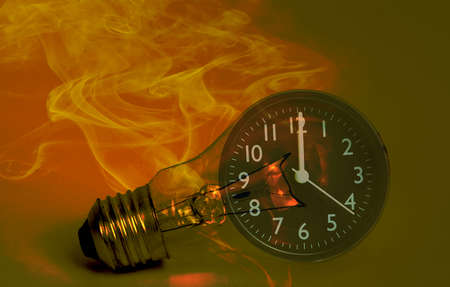 Abstract a light bulb with soot from working and a black analog clock. Show the concept of saving resources on the planet, reducing electricity consumption for future generations.の写真素材