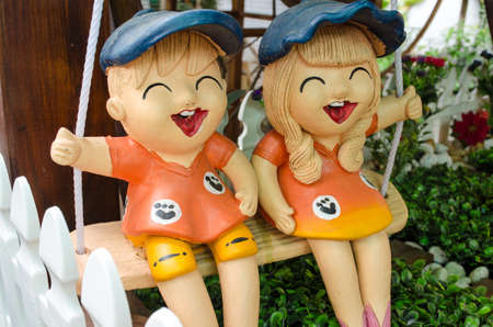 Ceramic Smile Boy and Girl Sitting Side by Side on a Swing in Gardenの写真素材