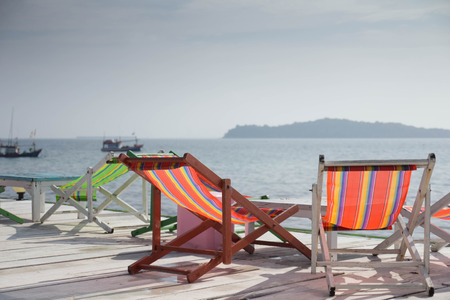 Colorful wooden sun beach summer chairs and table on the wooden white balcony with cloudy blue sky on island for relax on vacation holiday time.の写真素材