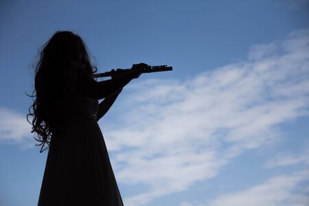 Asian Woman playing flute instrument in Silhouette shape with blue sky in background