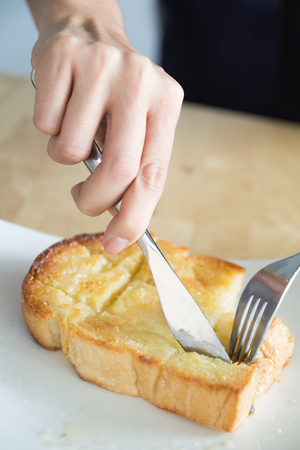 close-up hand use knife and fork which hand slice bread on Breakfast or coffee break time, toast bread topping with butter, sugar, milk or chocolate, very popular dessert serves with coffee, tea, milk or hot chocolate in coffee shop or restaurant on woodeの写真素材