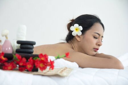 Asian woman lying down on white bed in spa salon with flowers, oil and equipment.の写真素材