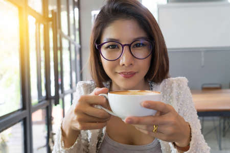 Young lady drinking coffee in cafe looking at you.
Business woman holding tea cup.
Portrait young female model with white mug in coffee shop enjoying leisure time alone, relaxing.の写真素材
