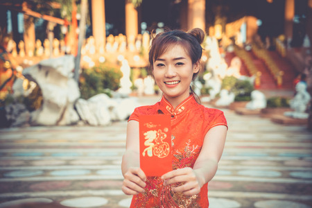 Chinese woman wearing traditional costume during Chinese New Year.Happy lady on culture season period. Female with China traditional dressing red cheongsam. Young girl smile Hands holding red envelope.の写真素材