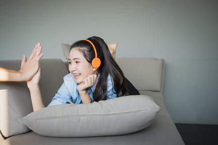 Young happy woman lying on sofa listening music with earphones. Girl relaxing at home. Giving high five, touching clapping hands.の写真素材
