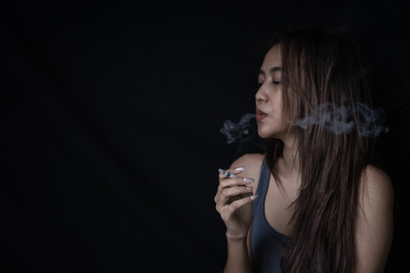 Young woman vaping, blowing cloud of smoke. Nicotine addiction toxic dangerous for healthy. Girl Smoking Cigarette on Black Background with copy space.の写真素材