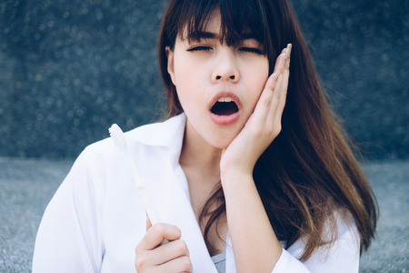 Young woman holding tooth brush hand touching cheek feeling pain. Oral problem.の写真素材