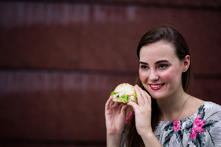Young girl holding fast food burger, American unhealthy calories. Hungry woman eating grilled hamburger in female hands.の写真素材