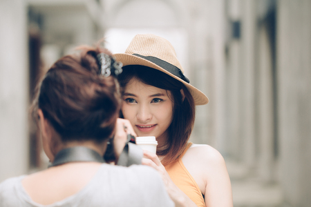 Woman photographer taking photos of young Asian model girl holding coffee cup.の写真素材