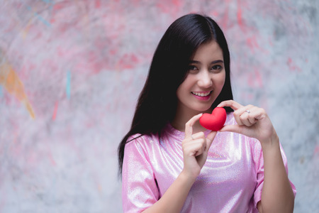 Young woman holding red heart on chest. Love sign symbol on background. Girl in love. love for life concept.の写真素材