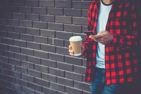 Hipster man holding mobile smart phone and coffee cup sending text message. communication connecting technology online concept with copy space.の写真素材
