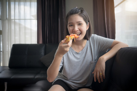 Happy girl eating pizza at home.
Beautiful young woman eating slice tasty pizza.
people order hot pizza delivery to home concept.の写真素材