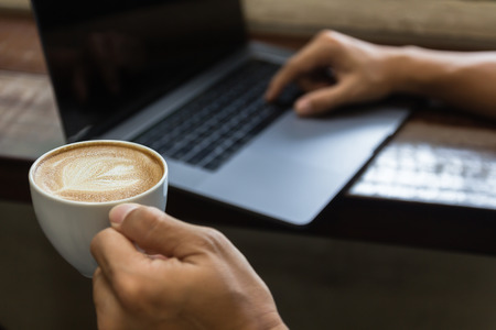 Close up man hand holding coffee cup and typing laptop computer. Business man working in coffee shop using notebook computer. Business technology lifestyle concept.の写真素材
