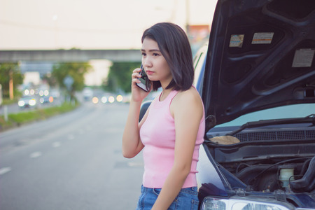 Young woman calling for assistance using mobile phone, after car broke down on the road side.の写真素材