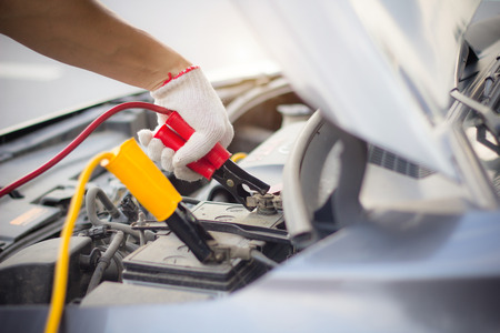 Car mechanic man using battery jumper cables to charge a dead battery.
Close up hand charging car battery with electricity red and yellow jumper cables. Car repair service concept.の写真素材
