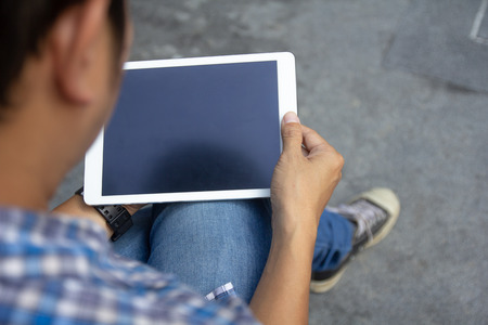 Top view mockup image of man hands holding and using white digital tablet pc with black blank desktop screen in hands while sitting on the floor, top view. Online internetの写真素材