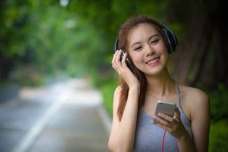 Happy young woman using smartphone relaxing and singing while listening music with earphones. Asian girl using headphones feeling heppiness concept. Beautiful Fashion Female model enjoying music.の写真素材