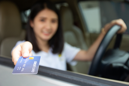 Young Asian girl driving car hand holding credit card payment for gas. Woman car owner paying fuel pump with credit card.の写真素材