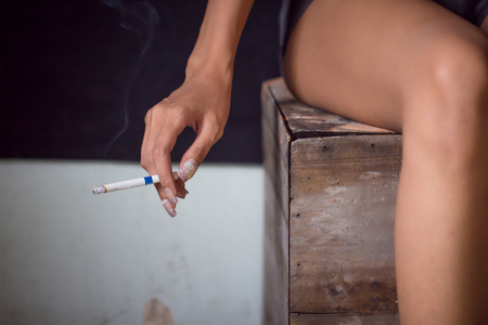Cigarette in smoking woman hand.Close up girl hand holding cigarette with smoke in dark room with copy space.の写真素材