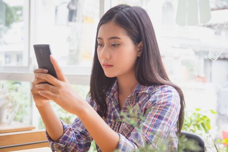 Young woman typing text message on smart phone in modern cafe. Asian girl sitting at table using mobile phone. 
female reading sms on mobile phone at coffee shop. business, online shopping, transfer money, financial, internet banking concept.の写真素材