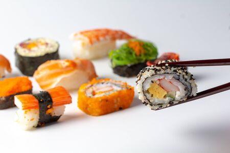 Eating fresh Sushi Maki and Niguiri roll menu with chopsticks. Sushi roll japanese food in restaurant. California Sushi roll set with vegetables and caviar closeup on white background.の写真素材