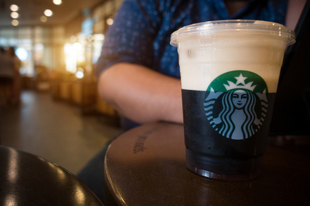 Chiangmai ,Thailand-July 22, 2019 : Sparkling Nitro Cold Brew Coffee shot in plastic take away cup ready to drink at Starbucks Store cafe. Starbucks coffee brand logo on Nitro americano coffee cold brew beverage on table with man sitting in background.のeditorial素材
