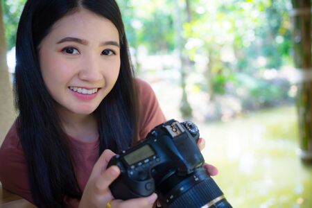 Woman photographer holding dslr camera in hands,  looking at camera.
Young happy asian girl professional photographer with dslr camera at summer green park outdoor.の写真素材