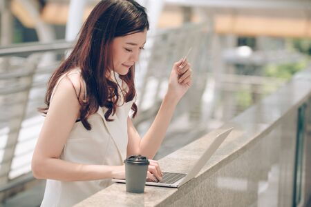 Business woman hand holding credit card using laptop shopping online.
Young happy Asian girl typing on notebook computer paying online by credit cards.
Online payment, internet banking, people and technology concept.の写真素材
