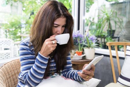 Young asian Woman drinking coffee and using mobile smartphone in the morning. Technology lifestyle...
